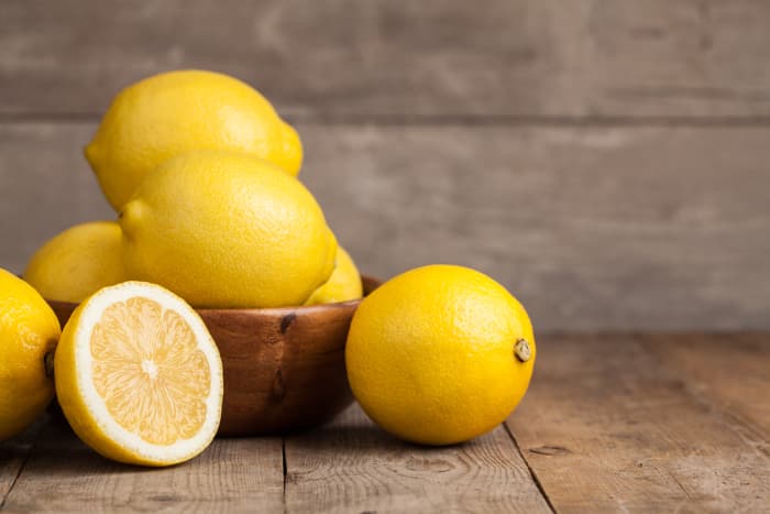  Ciotola di limoni interi con una metà di limone in primo piano.