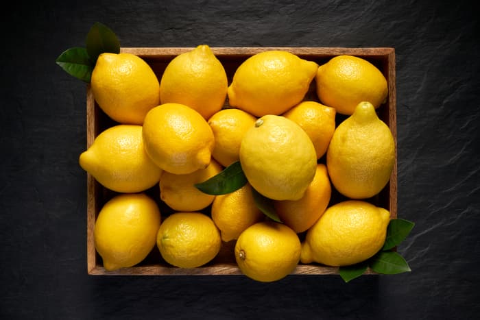  Draufsicht auf eine Schachtel Zitronen auf einer dunklen Oberfläche. Lemon Nutrition beschränkt sich nicht nur auf die Verwendung von Zitrone als Beilage für Gerichte - das Essen dieser Zitrusfrüchte hat viele gesundheitliche Vorteile.