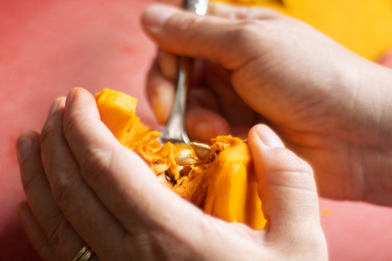 Hands using a spoon to scoop out the middle part of a pumpkin.