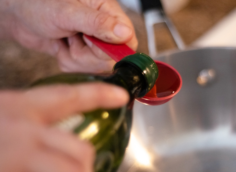 Hands pouring grape seed oil into a red measuring spoon.