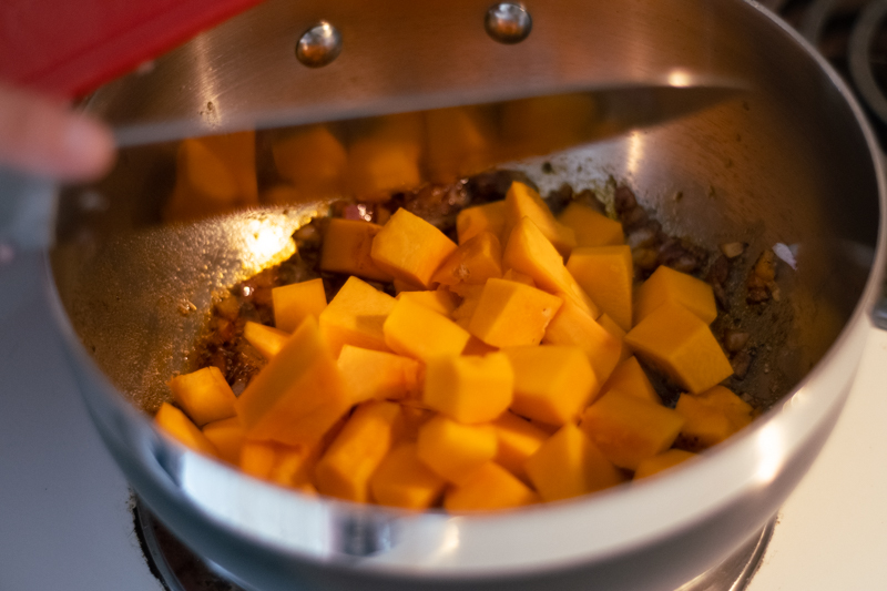 Pumpkin cubes added to cooked purple onions in a pan.