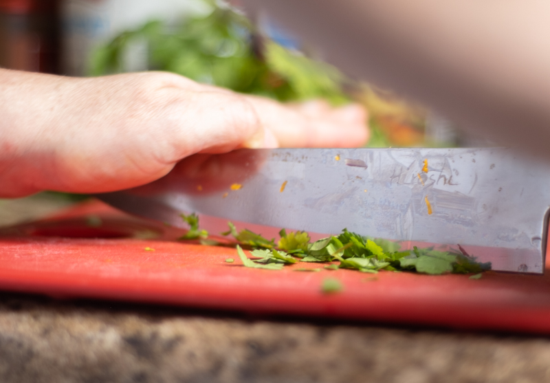Hands using a knife to chop cilantro leaves on a red cutting board.