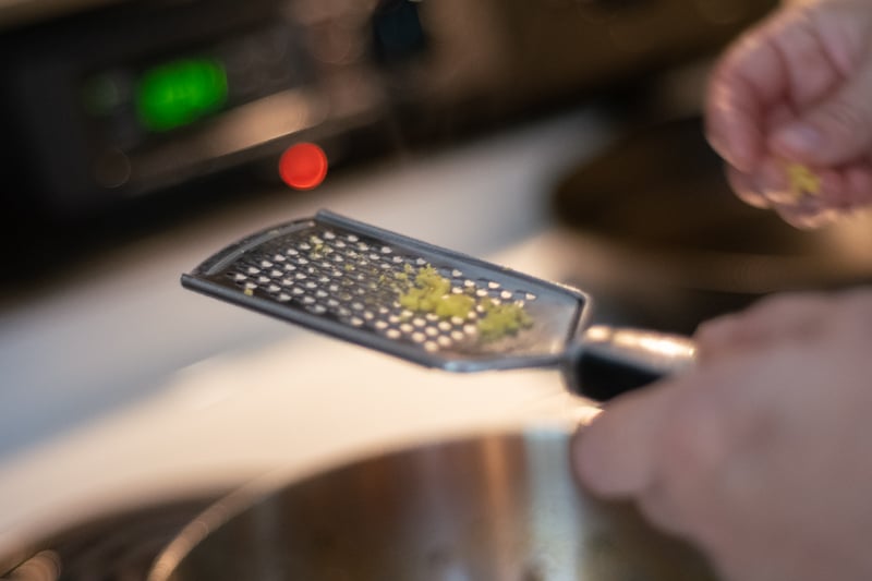 Hands using a grater to grate ginger into a pan.
