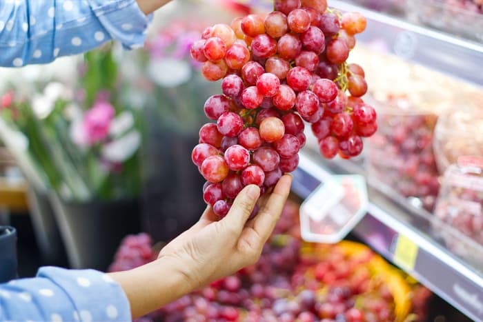 A woman holding a bunch of red grapes in a market.