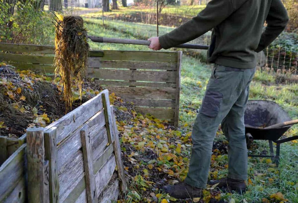 A man using a pitchfork to turn a compost pile.